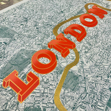 Load image into Gallery viewer, A close-up of a London city map print with large 3D red-orange letters spelling 'LONDON' and a gold River Thames running diagonally across the map.
