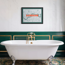 Load image into Gallery viewer, A framed art print of a London map hangs on a white marble-tiled wall above a white clawfoot bathtub with an ornate gold faucet. The wall features dark green paneling with gold trim, and patterned tiles decorate the floor.