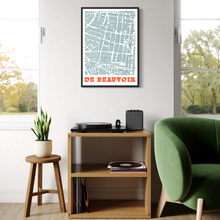Load image into Gallery viewer, A framed vintage-style street map print with the text 'DE BEAUVOIR' in orange and red hangs on a white wall above a wooden shelf in a styled living room with a green armchair, stool, plant, and record player.