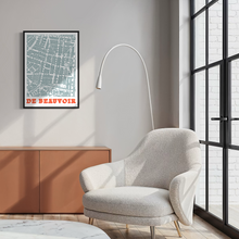 Load image into Gallery viewer, A framed street map art print of De Beauvoir Town, London, hangs on a light grey wall in a modern living room setting with a beige armchair, a white floor lamp, and a wooden cabinet.