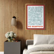 Load image into Gallery viewer, A framed vintage-style street map print reading 'DE BEAUVOIR' hangs on a wood-panelled wall above a bed, with a bedside table, lamp, and flowers visible in the room.
