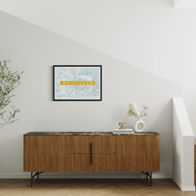 Load image into Gallery viewer, A framed art print featuring a light green map of Hampstead with bold yellow lettering, displayed on a white wall above a mid-century modern wooden sideboard in a styled interior setting.