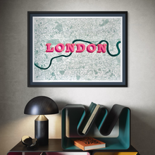 Load image into Gallery viewer, Framed wall art featuring a stylised London map with the word 'LONDON' in pink letters and a dark green Thames River, displayed above a console table with a lamp and books.
