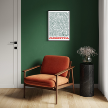 Load image into Gallery viewer, A framed street map print of Clerkenwell, London on a dark green wall in a modern room setting with an orange armchair and a black marble side table.
