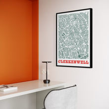Load image into Gallery viewer, A framed city map print of Clerkenwell hanging on a white wall in a modern room with an orange accent wall, a white desk, and a chair.
