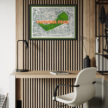 Load image into Gallery viewer, A framed vintage-style map print of Victoria Park, featuring a green park area and orange lettering, displayed on a slatted wood wall above a desk with a chair and lamp.
